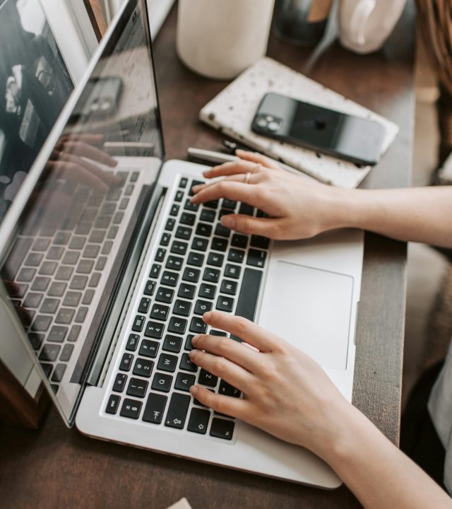 From above of unrecognizable woman sitting at table and typing on keyboard of computer during remote work in modern workspace